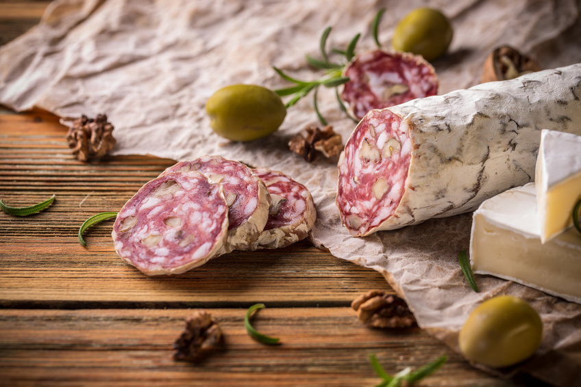 French salami with walnuts on craft paper on wooden background